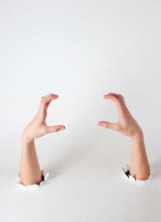 Female hands through the torn holes of a white background. Copy space. Creative artの写真素材