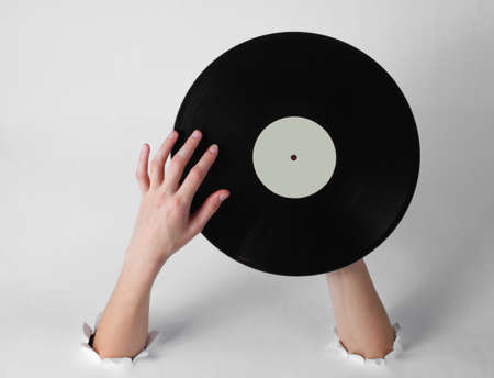 Female hands rotates a vinyl record through the torn holes of a white background. Creative art. Retro styleの写真素材