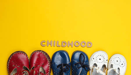 Lot of children's leather shoes on a yellow background with word childhood. Top view