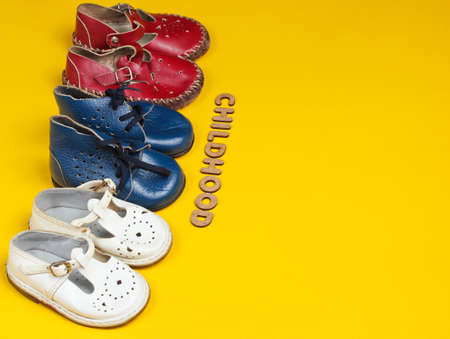 Lot of children's leather shoes on a yellow background with word childhood