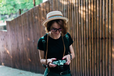 Stylish hipster woman in hat and glasses walking outdoors and use retro camera