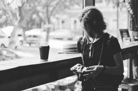 Young hipster woman holds a retro camera in her hands and adjusting the settings in old cafe
