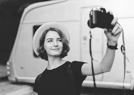 Stylish hipster woman in hat makes selfie portrait using retro camera. Black and white photoの写真素材
