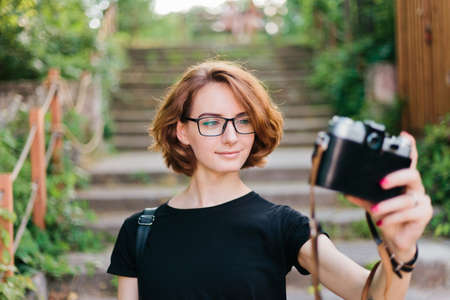 Young attractive hipster girl woman takes selfie portrait with retro camera outdoorsの写真素材