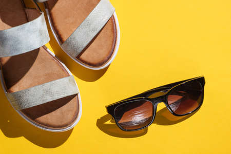 Fashionable women's sandals with sunglasses on a yellow background. Summer accessoriesの写真素材