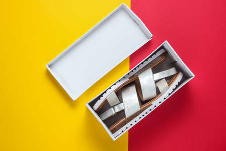 New women's leather sandals in a box on a red-yellow background. Top view. Minimalistic fashion still lifeの写真素材