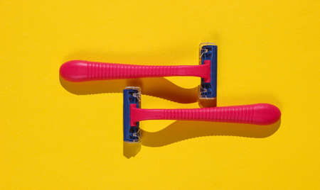 Two red plastic razors on yellow background. Minimalistic beauty and fashion concept
