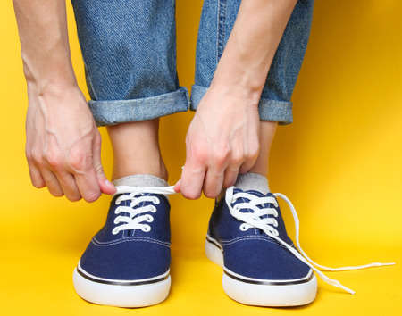 Woman tying shoelace of fashionable hipster sneakers over yellow background