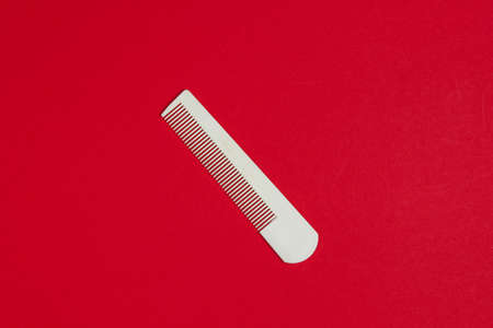 White plastic comb on red background. Hair care, beauty concept. Top view