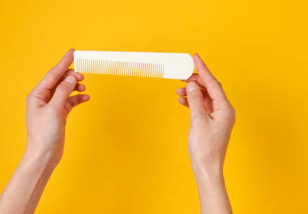 Female hands holding white plastic comb on yellow background. Hair care, beauty concept. Top viewの写真素材