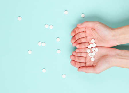 Many white tablets in the palm of hands on blue background. Medical minimalistic concept. Top view