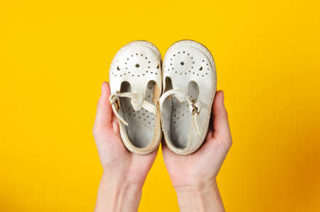 Motherhood, childhood concept. Children's leather sandals in the palms of female hands on yellow...