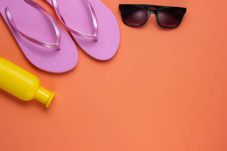 Summer still life. beach accessories. Fashionable beach pink flip flops, sunblock bottle, sunglasses, seashell on coral paper background. flat lay. copyspace. top viewの写真素材