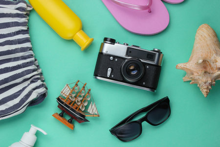 Summer still life. Beach accessories. Fashionable pink flip flops, bag, retro camera, sunblock bottle, sunglasses, seashell on blue paper background. Flat lay. Top viewの写真素材