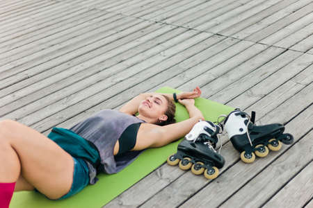 Tired but happy woman roller skater resting lying on mat outdoorsの写真素材
