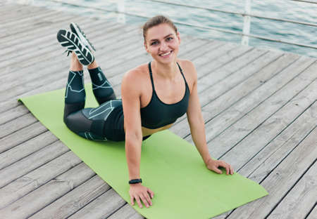 Portret Young fit woman in sportswear lying on a mat on a wooden terrace on the beach. Healthy...