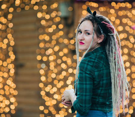 Youn informal woman with dreadlocks hairstyle and plaid shirt  against the background of garlands