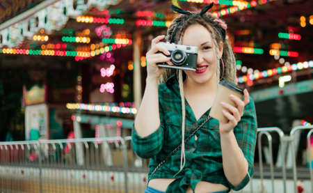 An informal young woman with dreadlocks takes pictures with retro camera in amusement park.の写真素材