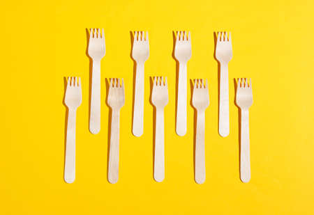 Many eco-friendly wooden forks on yellow background. Minimalistic eco concept. Pop art