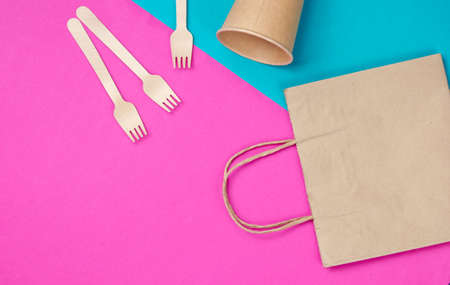 Disposable kitchenware of natural materials. Eco friendly concept. Wooden forks, empty craft coffee cup, bag on blue pink background. Top viewの写真素材