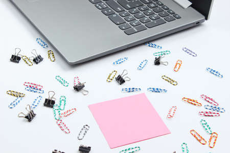 Minimalistic office still life. Laptop, stationery (paper clips, felt-tip pen, memo piece of paper) on white background. Studio shot.の写真素材