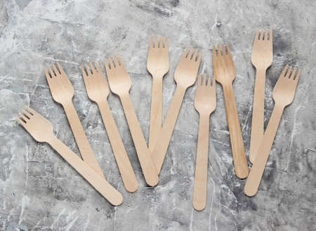 Many eco-friendly wooden forks on gray concrete background.