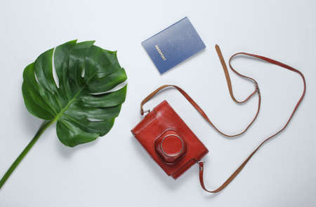 Traveled minimalistic still life. Monstera leaf, retro camera in cover, passport on a white background. Top viewの写真素材