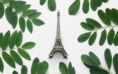 Figurine of the Eiffel tower on a white background with green leaves. Top view