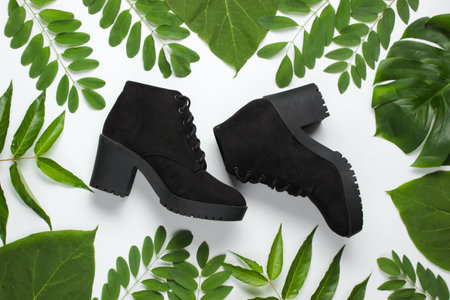 Suede black boots on a white background with green leaves. Eco shoesの写真素材