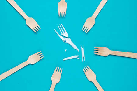 Minimalistic ecologically clean still life. Pop Art. Broken plastic fork among many wooden forks on blue background. Cutlery made from natural materialsの写真素材