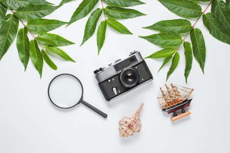 Retro style travel still life. Film camera, shells, green tropical leaves. Traveler accessories on a white background. Top viewの写真素材