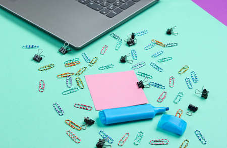Minimalistic office still life. Laptop, stationery (paper clips, felt-tip pen, memo piece of paper) on blue background. Studio shot.の写真素材