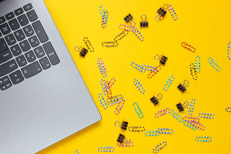 Minimalistic office still life. Laptop, paper clips on yellow background. Studio shot. Top viewの写真素材