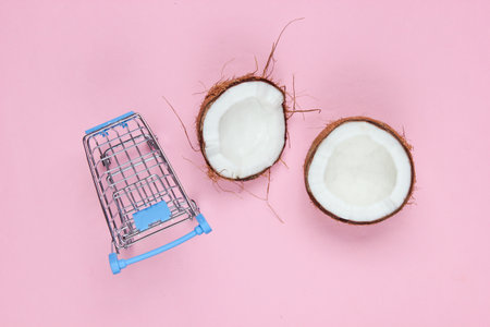 Fruit shopping concept. Shopping trolley, halves of broken coconut on a pink background. Top view