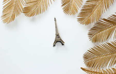 Minimalistic fashion still life. Eiffel tower figurine among decorative golden palm leaves on a white background. Top viewの写真素材