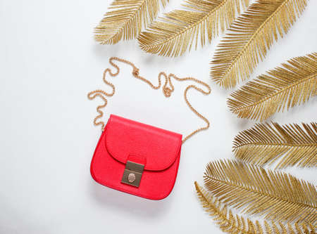 Minimalistic fashion still life. Leather red bag among decorative golden palm leaves on white background. Top viewの写真素材