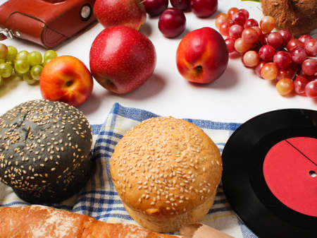 Retro style picnic food (baguette, rolls, fruit, grapes) vinyl record, film camera on a white...