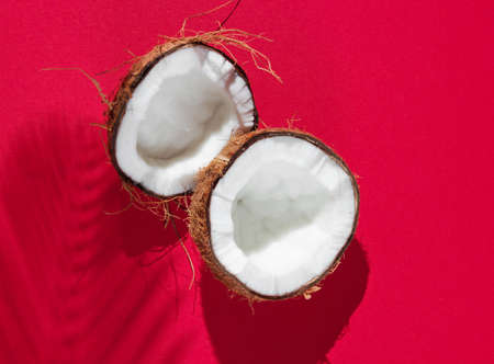 Minimalistic tropical still life. Two halves of chopped coconut with shadows from palm leaves on red...