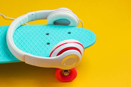 Hipster outfit. Skateboard with headphones on yellow background. Creative fashion minimalism. Trendy old fashionable style. Minimal summer fun. Music conceptの写真素材