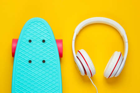 Hipster outfit. Skateboard with headphones on yellow background. Creative fashion minimalism. Trendy old fashionable style. Minimal summer fun. Music conceptの写真素材