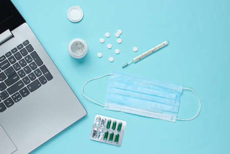 Medical background. Workspace of a modern doctor. Laptop, pills, gauze mask, thermometer on a blue background. Top view. Flat layの写真素材