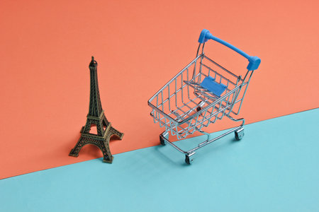 Shopping in Paris minimalistic concept. Shopping trolley, eiffel tower figurine on coral blue background.の写真素材