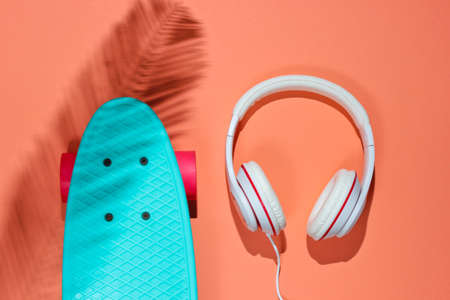 Hipster outfit. Skateboard with headphones on coral background with shadow from palm leaf. Creative fashion minimalism. Trendy old fashionable style. Minimal summer fun. Music conceptの写真素材