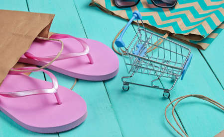 Summertime sale. Shopping concept. Summer beach accessories (flip flops, sunglasses), mini shopping trolley on a blue wooden background.の写真素材