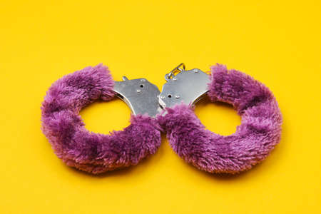 Handcuffs for sex games on yellow background. Sexual bdsm toy. Fetish, erotic concept.の写真素材