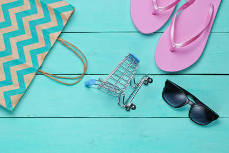 Summertime sale. Shopping concept. Summer beach accessories (flip flops, sunglasses), mini shopping trolley on a blue wooden background. Top view. Flat layの写真素材