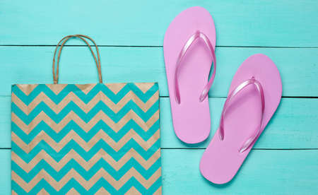 New pink flip flops and paper bag on blue wooden background. Shopping concept. Top viewの写真素材