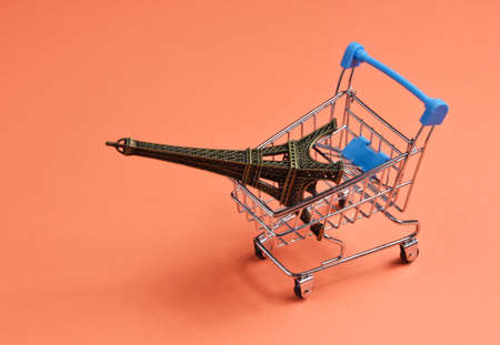 Shopping in Paris minimalistic concept. Shopping trolley, eiffel tower figurine on coral colored background.の写真素材