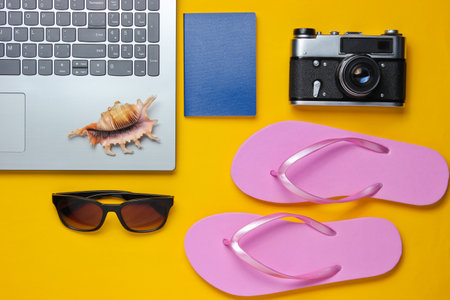 Summer leisure. Summertime relax.Laptop and travel accessories on yellow background. Studio short. Beach object. Top view. Flat layの写真素材