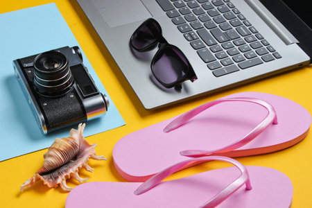 Summer leisure. Summertime relax.Laptop and beach accessories on yellow background. Studio short. Beach object.の写真素材